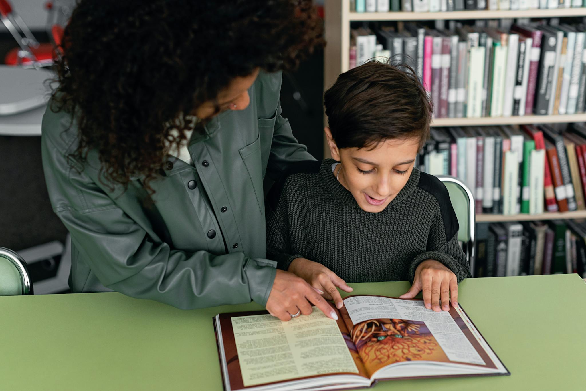 A teacher guides a child through a book in a cozy library setting.